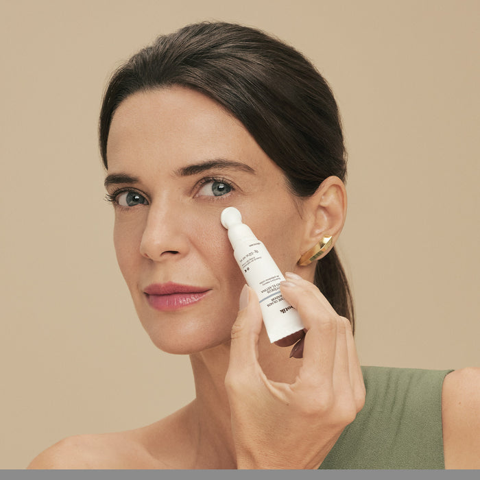 Woman applying Boticário Botik Peptídeos Pró-Elastina eye cream to the under-eye contour with the metal massaging applicator tip – Buy now at MKPBR.COM – Worldwide Shipping