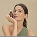 Model holding the 30 ml Boticário Botik Peptídeos Pró-Elastina Facial Serum bottle beside her face, showing the amber glass flacon – Buy now at MKPBR.COM – Worldwide Shipping
