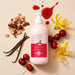 Boticário Cuide-se Bem Cereja de Fases body lotion bottle in a flat lay with cherries, vanilla pods, cedarwood chips, ylang-ylang flowers and a drop of cherry syrup – Buy now at MKPBR.COM – Worldwide Shipping