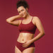 Woman in burgundy underwear resting her hand on her lower belly, Boticário Cereja de Fases Warming Body Oil cycle care lifestyle – Buy now at MKPBR.COM – Worldwide Shipping