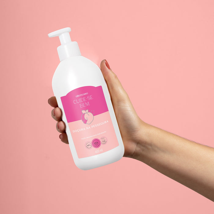 Hand holding the Boticário Cuide-se Bem Doçura na Pessegura 400 ml deodorant body lotion bottle against a pink background for scale – Buy now at MKPBR.COM – Worldwide Shipping