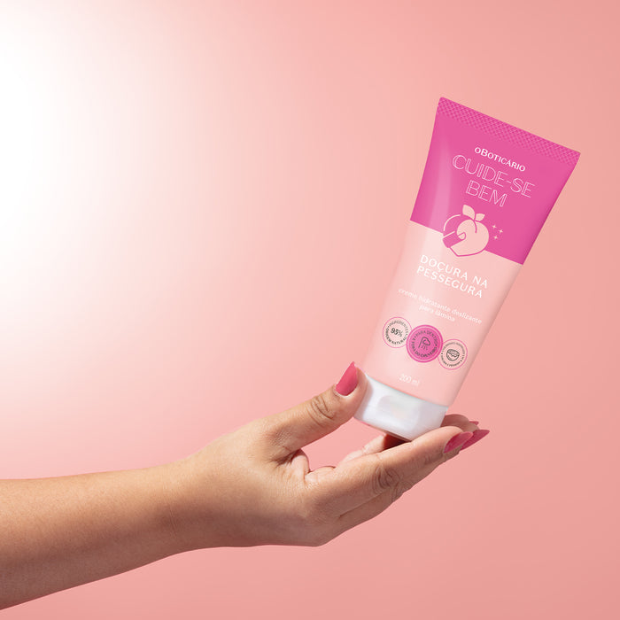 Hand holding the 200 ml Boticário Cuide-se Bem Doçura na Pessegura glide shaving cream tube against a pink background, showing the tube size – Buy now at MKPBR.COM – Worldwide Shipping