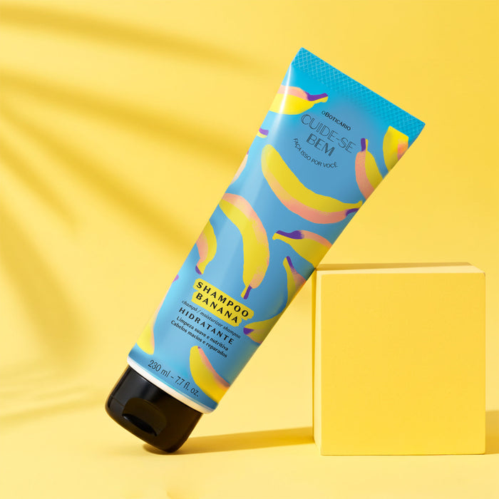 O Boticário Cuide-se Bem Feira Banana Shampoo tube leaning at an angle on a yellow studio block with the full front label in view – Buy now at MKPBR.COM – Worldwide Shipping