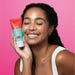 Smiling model holding the Boticário Cuide-se Bem Feira Morango facial scrub tube with pink strawberry scrub applied to her cheek – Buy now at MKPBR.COM – Worldwide Shipping