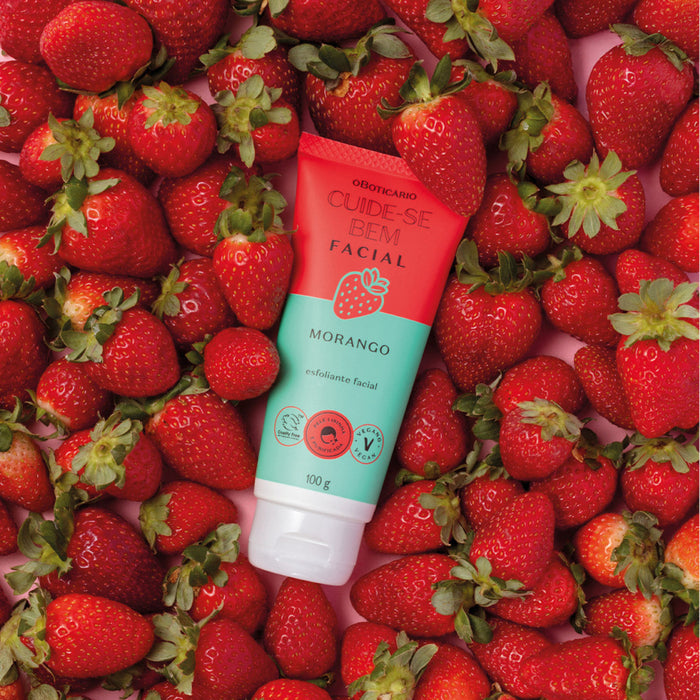 Boticário Cuide-se Bem Feira Morango facial scrub tube lying on a bed of fresh red strawberries – Buy now at MKPBR.COM – Worldwide Shipping