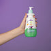 Hand holding the Boticário Dr. Botica Poção da Espuma Kids Shampoo for Coils 4ABC 400 ml bottle against a purple background, showing the ergonomic accessible pump design – Buy now at MKPBR.COM – Worldwide Shipping