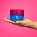 Hand holding the 250 g jar of Boticário Egeo Dolce Illusion gourmand deodorant body cream against a pink background – Buy now at MKPBR.COM – Worldwide Shipping