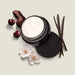 O Boticário Her Code Velvet Body Cream open jar surrounded by red fruits, sandalwood, vanilla pods and white blossom evoking the woody-fruity scent – Buy now at MKPBR.COM – Worldwide Shipping