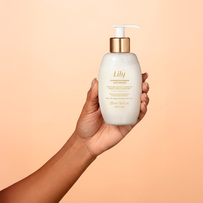 Hand holding the Boticário Lily Acetinado Satin Conditioner 250 ml bottle against a peach backdrop, showing its compact pump size – Buy now at MKPBR.COM – Worldwide Shipping