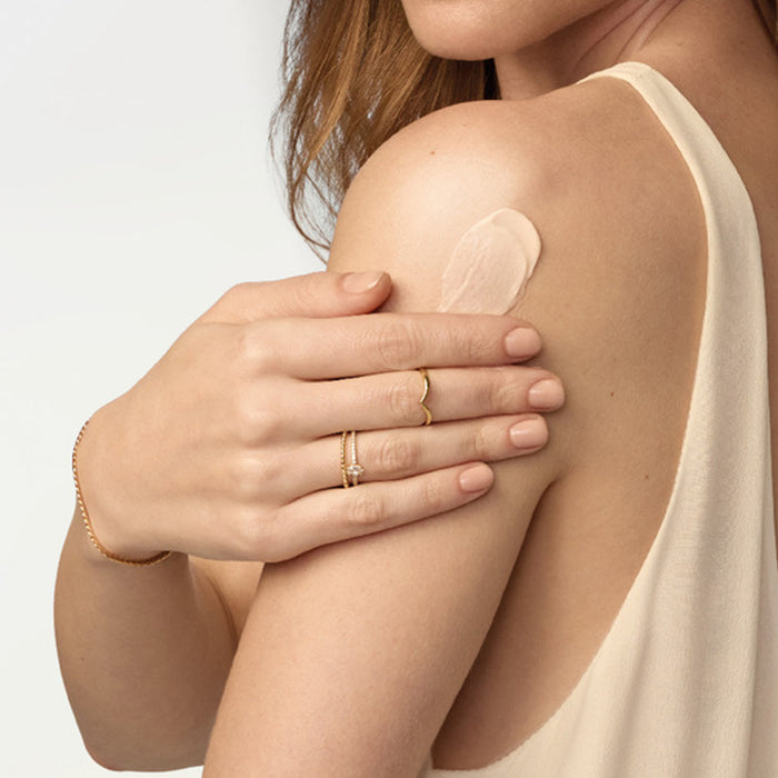 Woman smoothing Boticário Lily Cashmere Satin Body Cream onto her shoulder, showing the rich satin texture on skin – Buy now at MKPBR.COM – Worldwide Shipping