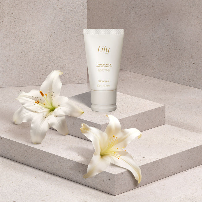 O Boticário Lily Satin Hand Cream 50 g tube on a stone pedestal beside fresh white lily blooms, Brazilian floral hand care – Buy now at MKPBR.COM – Worldwide Shipping