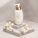 Boticário Lily Satin Shower Cream 250 ml bottle styled on a stone podium beside fresh white lily flowers – Buy now at MKPBR.COM – Worldwide Shipping