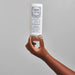 Hand holding the Boticario Match Ciencia das Curvas Conditioner and Leave-In 300 ml bottle upside down against a grey background, showing bottle size and flip-top cap – Buy now at MKPBR.COM – Worldwide Shipping