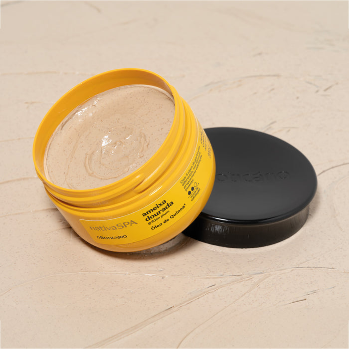 Open jar of Boticário Nativa SPA Ameixa Dourada exfoliating body cream lying beside its black lid on a beige textured backdrop, scrub cream visible inside – Buy now at MKPBR.COM – Worldwide Shipping