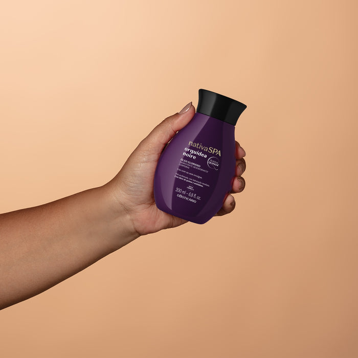 Hand holding the Boticário Nativa SPA Orquídea Noire body oil bottle against a warm beige background, showing its compact 200 ml size – Buy now at MKPBR.COM – Worldwide Shipping