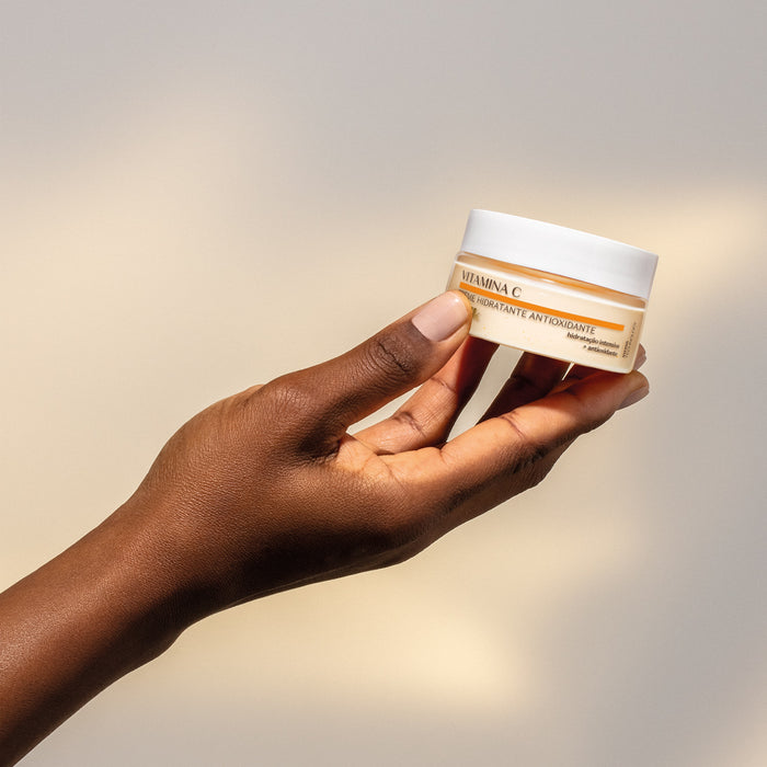 Hand holding the O Boticário Botik Vitamina C Antioxidant Face Moisturizer 50 g jar, showing the compact travel-friendly size of the Brazilian antioxidant face cream – Buy now at MKPBR.COM – Worldwide Shipping