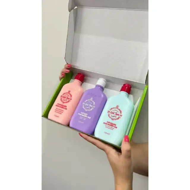 A person's hands holding the Gold Spell Co. Cronoterapia Box open, revealing the three pastel-colored 250ml hair masks inside for personalized hydration, nutrition, and reconstruction treatment - Buy now at MKPBR.COM - Worldwide Shipping