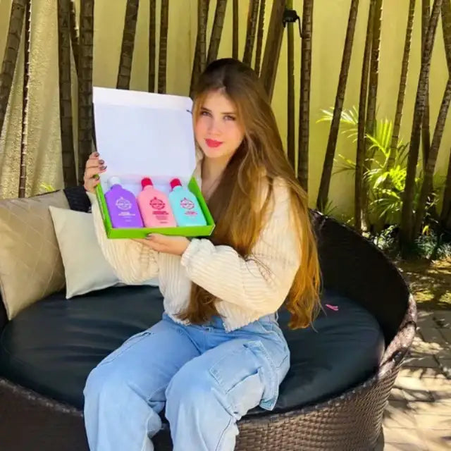 Smiling woman presenting the open Gold Spell Co. Cronoterapia Box with the three colored hair masks neatly arranged inside, in an outdoor setting – Buy now at MKPBR.COM - Worldwide Shipping