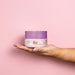 Hand holding the Boticário Liz D'Essence 250 g body cream jar against a soft pink background for scale – Buy now at MKPBR.COM – Worldwide Shipping