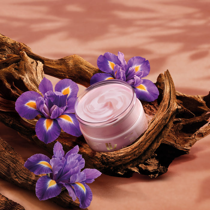 Open jar of Boticário Liz D'Essence body cream showing pink cream, styled with purple iris flowers and driftwood – Buy now at MKPBR.COM – Worldwide Shipping