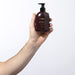 Hand holding the Boticário Malbec Pure Gold deodorant body lotion 200 ml pump bottle, showing the compact travel-friendly size – Buy now at MKPBR.COM – Worldwide Shipping