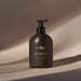 Boticário Malbec Pure Gold deodorant body lotion pump bottle photographed in warm directional light on a neutral beige backdrop – Buy now at MKPBR.COM – Worldwide Shipping