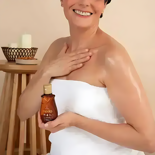 Woman applying Paixão Avelã (Hazelnut) body oil to shoulder with a dewy finish. Buy now at MKPBR.COM – Worldwide Shipping