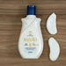 White Paixão Inspiradora Rosas Brancas 24h Deo Hydrating Lotion with almond oil, front bottle on wood with two creamy swatches. Buy now at MKPBR.COM – Worldwide Shipping
