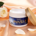 Open jar of Paixão Inspiradora Rosas Brancas hydrating lotion on peach satin with a white rose and petals. — Buy now at MKPBR.COM – Worldwide Shipping