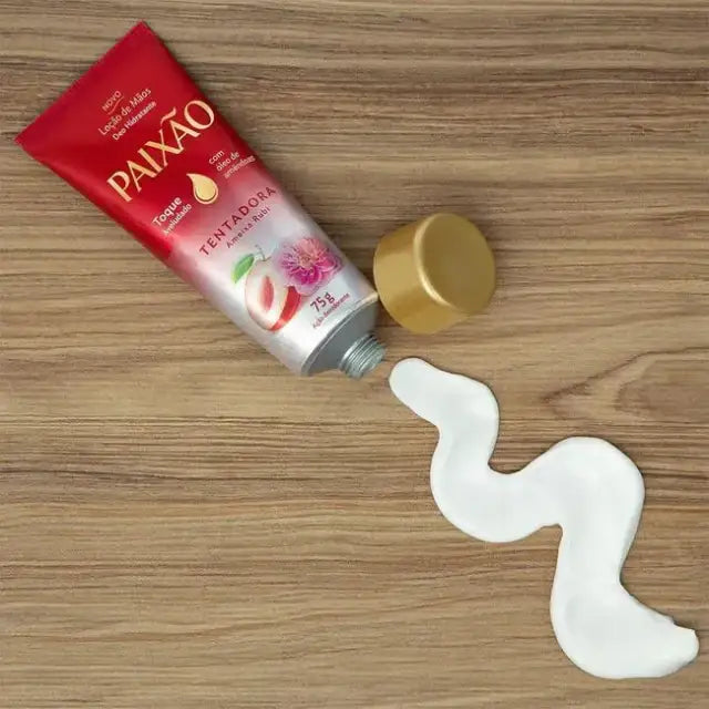 Red tube of Paixão Tentadora 'Ameixa Rubi' Hand Cream 2.5 fl oz (75 g) with white cream squeezed out onto a light wooden surface, highlighting its smooth texture – Buy now at MKPBR.COM – Worldwide Shipping