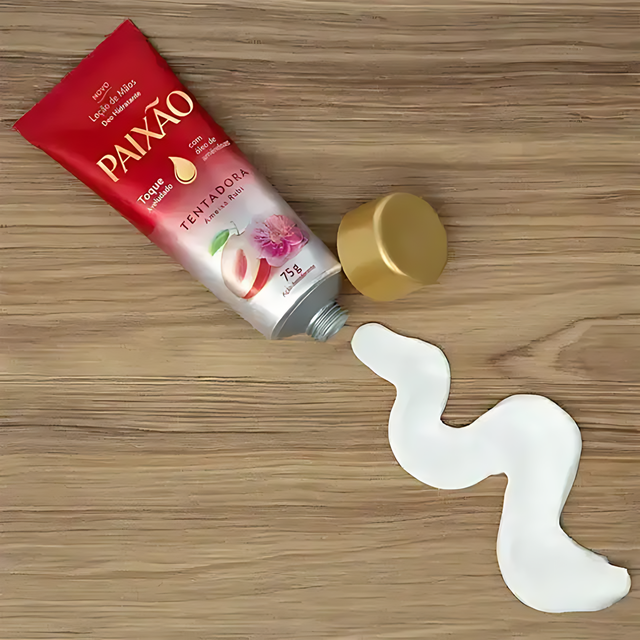 Red tube of Paixão Tentadora 'Ameixa Rubi' Hand Cream 2.5 fl oz (75 g) with white cream squeezed out onto a light wooden surface, highlighting its smooth texture – Buy now at MKPBR.COM – Worldwide Shipping