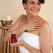 Woman applying Paixão Tempting Ruby Plum body oil on shoulder. Buy now at MKPBR.COM – Worldwide Shipping