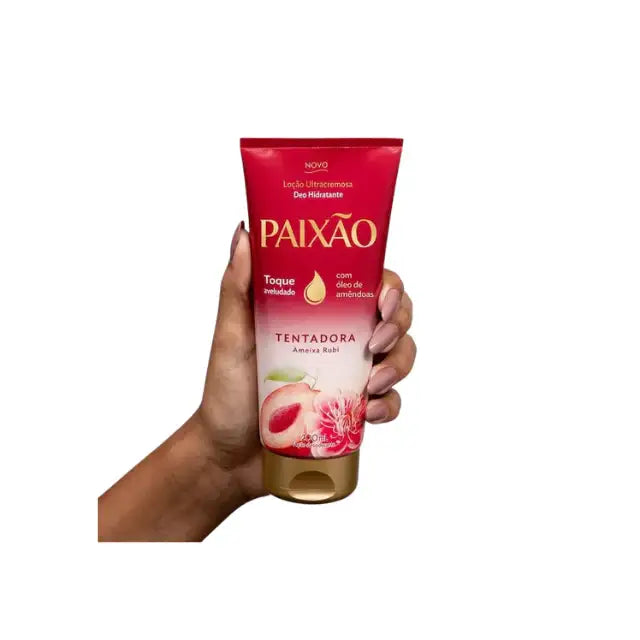 Hand holding a Paixão Tentadora Ultracremosa Deo Hidratante lotion tube with red and gold packaging featuring ruby plum and almond oil. Buy now at MKPBR.COM – Worldwide Shipping