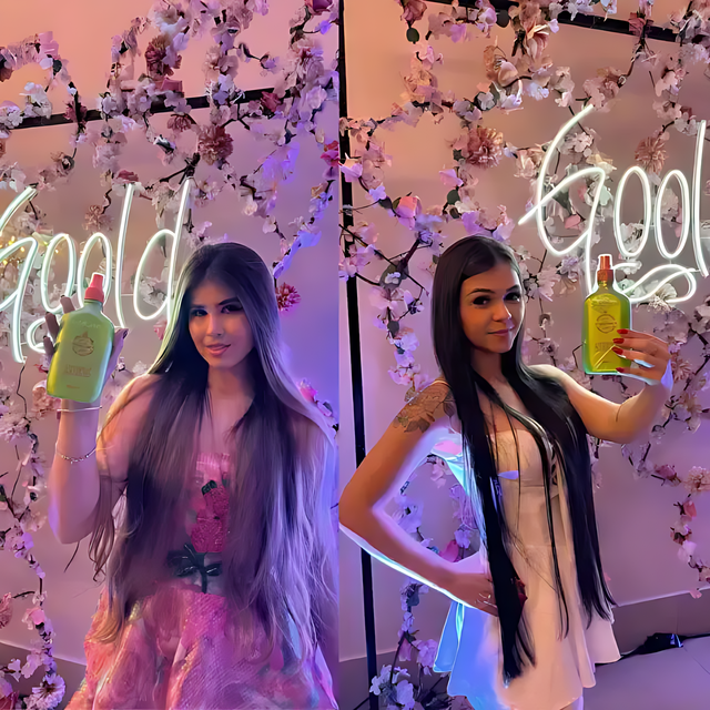 Two models holding Gold Spell Receitinha Poderosa hair tonic 250ml bottles at floral event backdrop - Buy now at MKPBR.COM - Worldwide Shipping